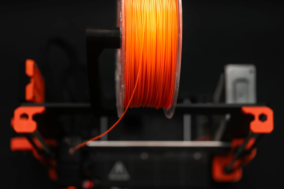 Narancssárga filamenttekercs, amely egy 3D nyomtatóba tölti be az anyagot